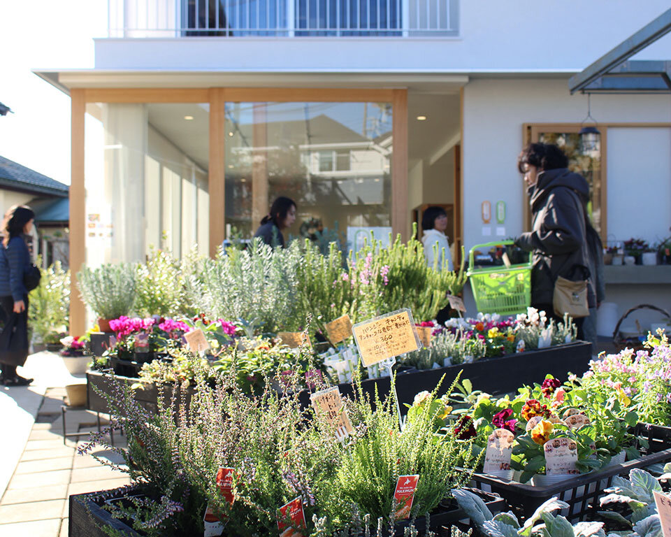 街ノ停留所の花棟外観。カラフルな花苗が並ぶ「花ノ停留所」で買い物を楽しむ来店客の様子。